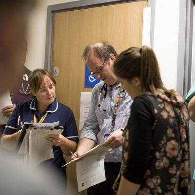 A doctor and a Matron check patient information in a team meeting