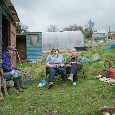 Three people laughing while sat having a break in their allotment