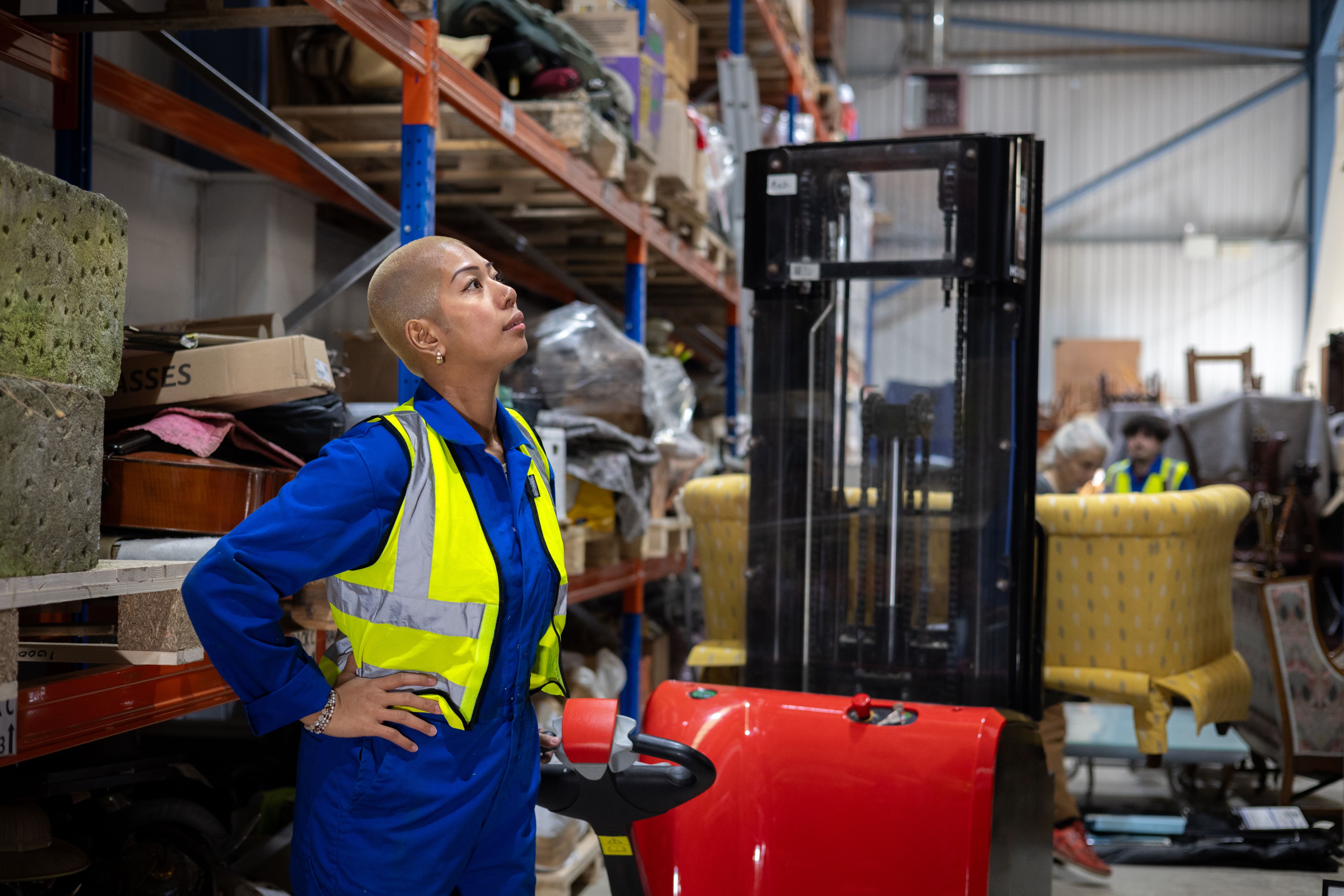 A woman in a high-vis jacket stands in a warehouse, resting her hands on her hips.
