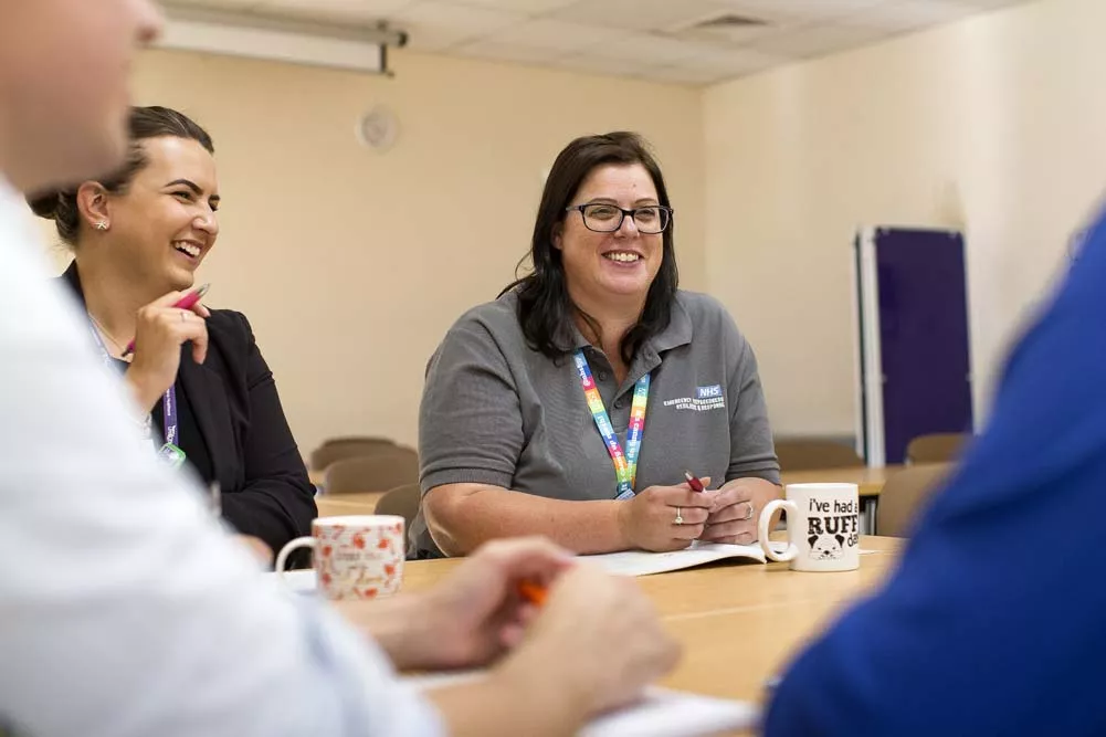 NHS staff member wearing glasses and smiling in a meeting