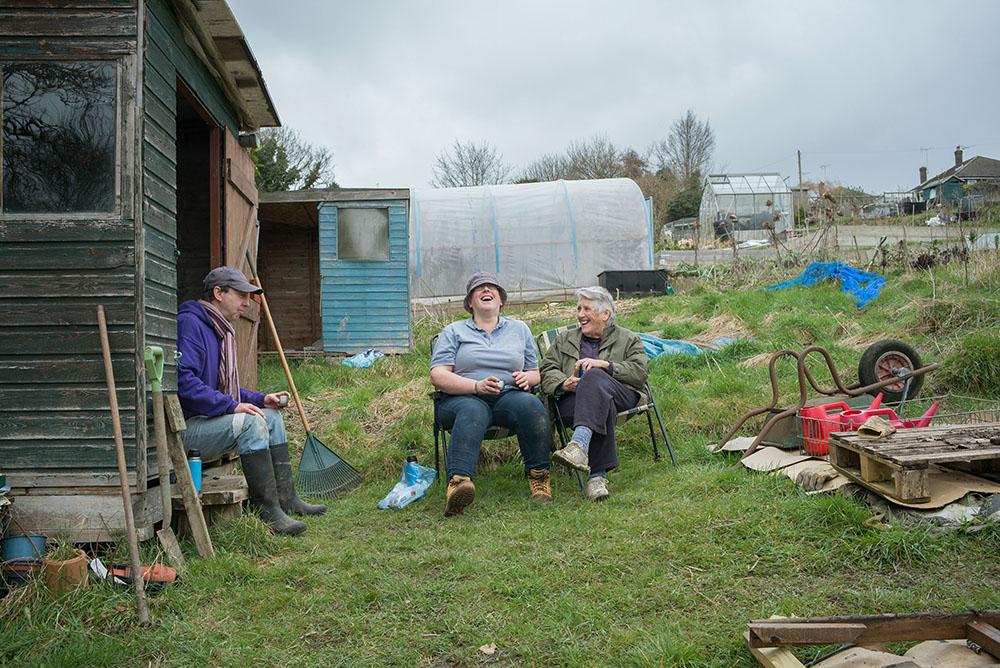 Three people laughing while sat having a break in their allotment