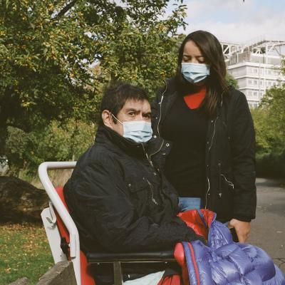 Photo showing two people in face masks, one in a wheelchair and one standing