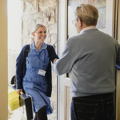 A nurse greets at a patient at the door of his home