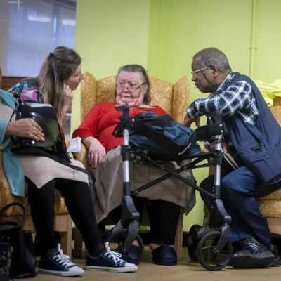 Two older people talk to a younger person whilst sat in a communal area