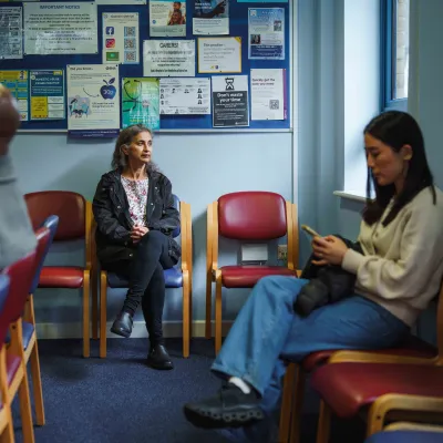 A woman sits in a GP practice waiting room.