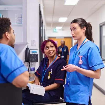 Three nurses talk in a hospital ward reception area